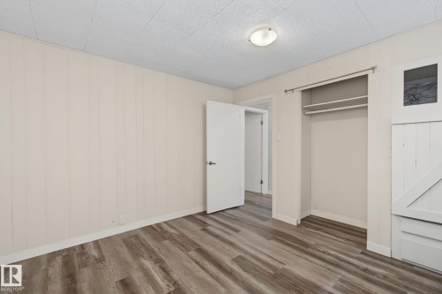 Room featuring wood-finish flooring, vertical paneling on walls, a built-in open closet with shelving, and a ceiling-mounted light fixture - 9545 65 Avenue, Edmonton, AB 