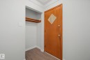 Entryway featuring a wood-finish door with diamond-shaped inset, wood-finish flooring, and a built-in closet with shelving and hanging rod - 9545 65 Avenue, Edmonton, AB 