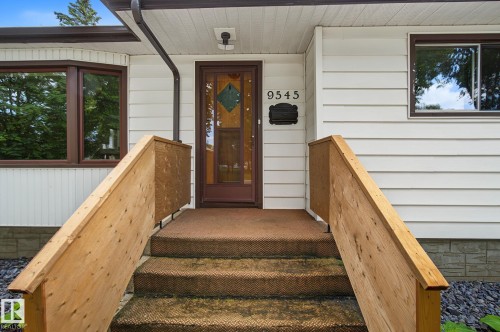 Exterior featuring white siding, a brown entry door with decorative glass, and a bay window with brown trim - 9545 65 Avenue, Edmonton, AB 