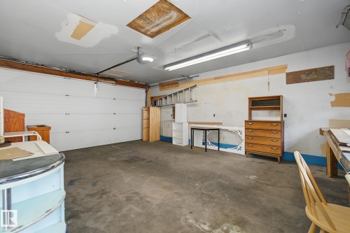 Spacious garage with a sectional overhead door, concrete flooring, and ceiling-mounted fluorescent lighting - 9545 65 Avenue, Edmonton, AB 