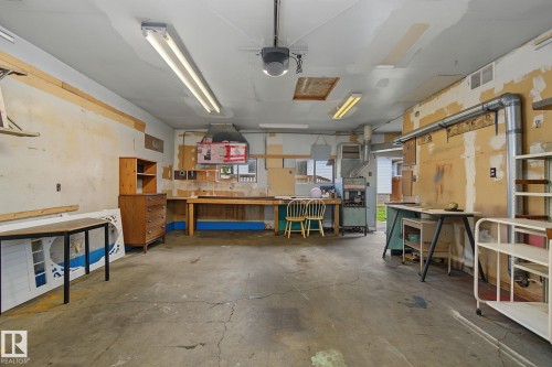 Spacious garage featuring a concrete floor, overhead fluorescent lighting, and built-in wood workbenches - 9545 65 Avenue, Edmonton, AB 
