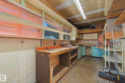 Workshop space featuring extensive open shelving, a built-in workbench, and multiple windows with horizontal blinds - 9545 65 Avenue, Edmonton, AB 