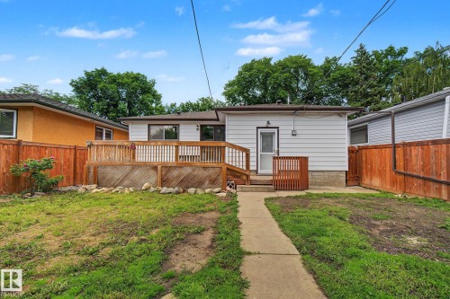 Rear exterior with a wooden deck featuring lattice skirting, a white siding facade, a side entry door, and a concrete path - 9545 65 Avenue, Edmonton, AB 