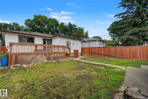 Rear exterior featuring a wood deck with lattice skirting, wood privacy fencing, and a concrete pathway - 9545 65 Avenue, Edmonton, AB 