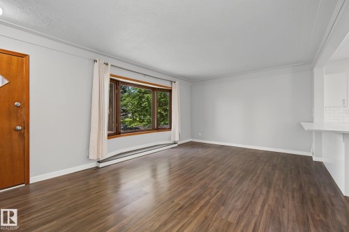Spacious living area featuring wood-finish flooring, light gray wall tones, and crown molding - 9545 65 Avenue, Edmonton, AB 
