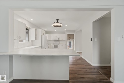 Modern kitchen with a breakfast bar, white cabinetry, integrated appliances, recessed lighting, and wood-finish flooring - 9545 65 Avenue, Edmonton, AB 