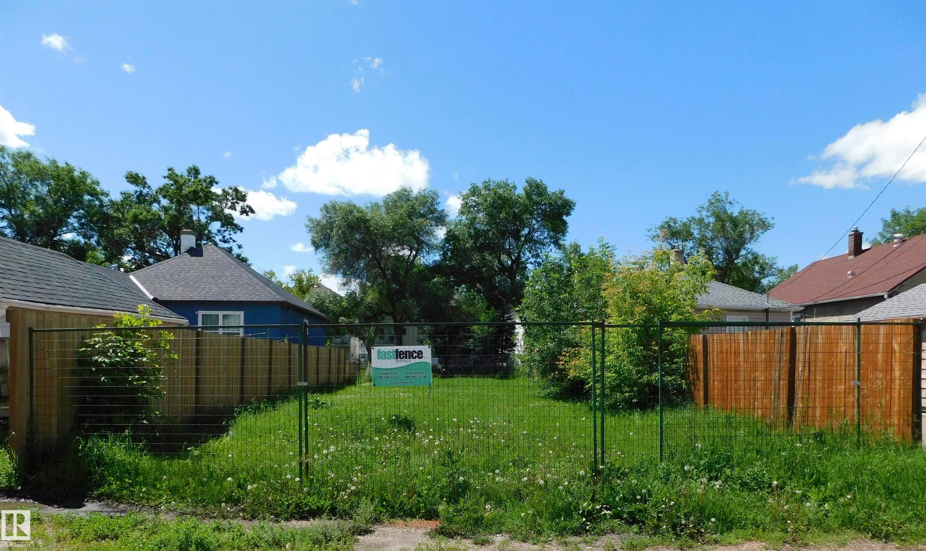 Vacant lot featuring a chain-link fence, partial wood fencing, and mature trees - 11715 97 Street, Edmonton, AB