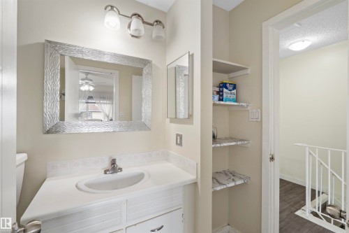 Bathroom vanity with a white countertop and integrated sink, complemented by a decorative framed mirror and a three-light fixture - 173 Tudor Lane, Edmonton, AB 