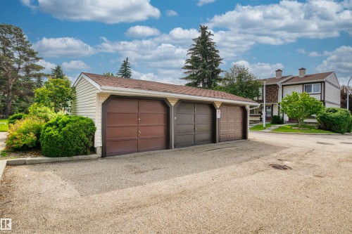 Detached garage structure featuring three individual garage doors, light-colored siding, and a brown shingle roof - 173 Tudor Lane, Edmonton, AB 