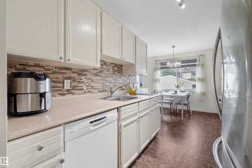 Kitchen featuring white cabinetry, a mosaic tile backsplash, a stainless steel sink, and wood-finish flooring - 173 Tudor Lane, Edmonton, AB 