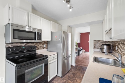 Kitchen featuring white cabinetry, stainless steel appliances, a multi-tone tile backsplash, light-toned countertops, and wood-finish flooring - 173 Tudor Lane, Edmonton, AB 