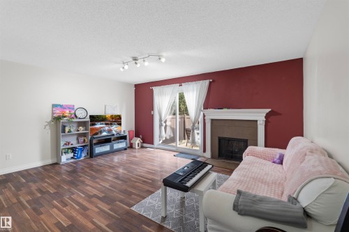 Spacious living area featuring wood-finish flooring, a decorative fireplace with a mantel, and a sliding glass door providing exterior access - 173 Tudor Lane, Edmonton, AB 