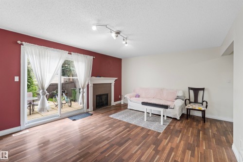 Living space featuring wood-finish flooring, a fireplace with a mantel, track lighting, and a sliding glass door providing access to an outdoor patio - 173 Tudor Lane, Edmonton, AB 
