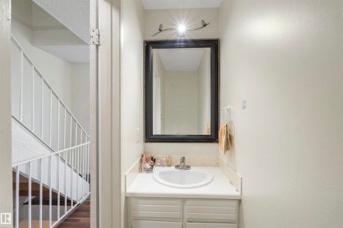 Bathroom vanity with an integrated sink, framed mirror, wall-mounted light fixture, and built-in cabinetry - 173 Tudor Lane, Edmonton, AB 
