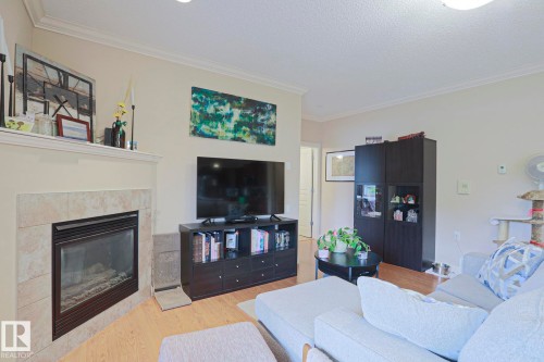 Living area featuring a corner fireplace with a tile surround and mantel, wood-finish flooring, recessed lighting, and crown molding - 13 7293 South Terwillegar Drive, Edmonton, AB 