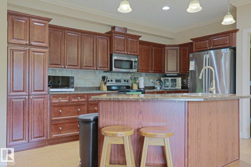 Kitchen featuring an expansive island with breakfast bar seating, stainless steel appliances, abundant cabinetry, a tiled backsplash, and recessed lighting - 13 7293 South Terwillegar Drive, Edmonton, AB 