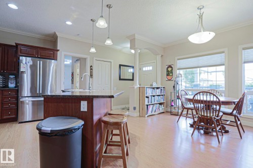 Open-concept kitchen and dining area featuring light wood-finish flooring, dark wood cabinetry, a center island with countertop, and stainless steel appliances - 13 7293 South Terwillegar Drive, Edmonton, AB 