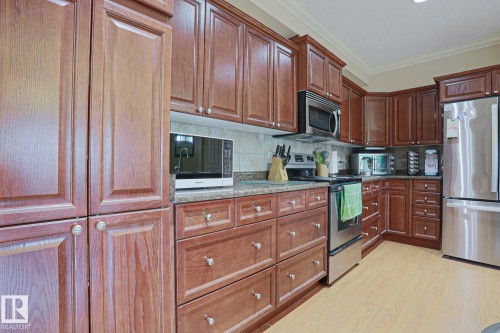 Kitchen featuring wood-finish cabinetry, stainless steel appliances, speckled countertops, a tile backsplash, and light wood-finish flooring - 13 7293 South Terwillegar Drive, Edmonton, AB 