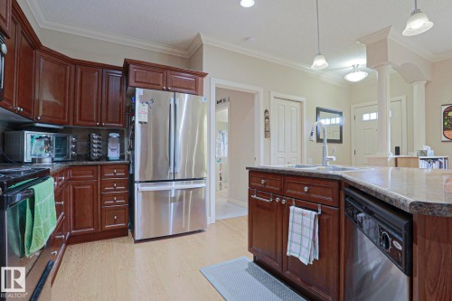 Kitchen featuring rich wood cabinetry, stainless steel appliances, light-toned flooring, pendant lighting, and a kitchen island with sink and integrated dishwasher - 13 7293 South Terwillegar Drive, Edmonton, AB 