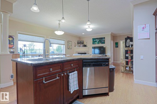 Kitchen island featuring a double basin sink with a gooseneck faucet, dark wood cabinetry, and a stainless steel dishwasher - 13 7293 South Terwillegar Drive, Edmonton, AB 