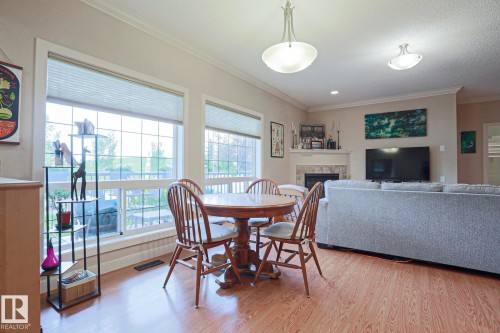 Open-concept living area featuring wood-finish flooring, large windows, a fireplace with a tile surround and mantel, crown molding, and recessed lighting - 13 7293 South Terwillegar Drive, Edmonton, AB 