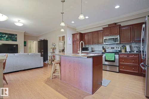 Kitchen featuring dark wood cabinetry, stainless steel appliances, a center island with a sink, and pendant lighting - 13 7293 South Terwillegar Drive, Edmonton, AB 