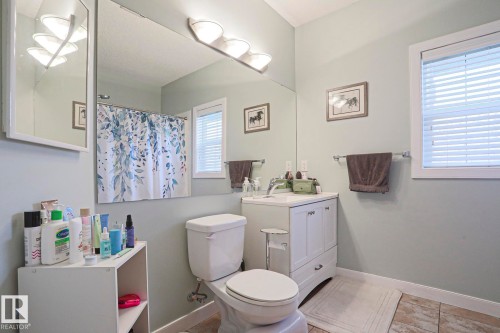 Bathroom featuring a white vanity with integrated sink, a wall-mounted mirror, and a window with blinds - 13 7293 South Terwillegar Drive, Edmonton, AB 