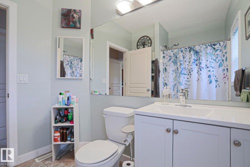 Bathroom featuring a white vanity with integrated sink, chrome faucet, wall-mounted mirror, and a toilet - 13 7293 South Terwillegar Drive, Edmonton, AB 