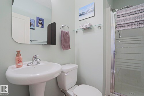 Pedestal sink with chrome faucet, framed by a rounded-edge wall mirror and a glass shower enclosure - 13 7293 South Terwillegar Drive, Edmonton, AB 
