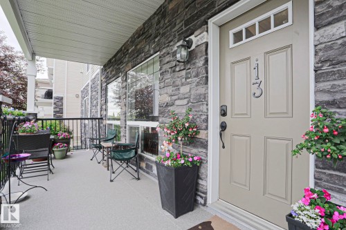 Inviting covered porch with stone veneer siding and an entryway door featuring a transom window - 13 7293 South Terwillegar Drive, Edmonton, AB 