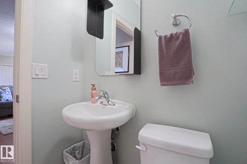 Pedestal sink with chrome faucet, wall-mounted mirror, and white toilet - 13 7293 South Terwillegar Drive, Edmonton, AB 