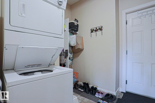 Dedicated laundry area featuring a stackable washer and dryer, tile flooring, and a paneled entry door - 13 7293 South Terwillegar Drive, Edmonton, AB 