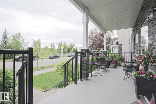 Covered front porch featuring a stone facade, white support columns, and black metal railings - 13 7293 South Terwillegar Drive, Edmonton, AB 