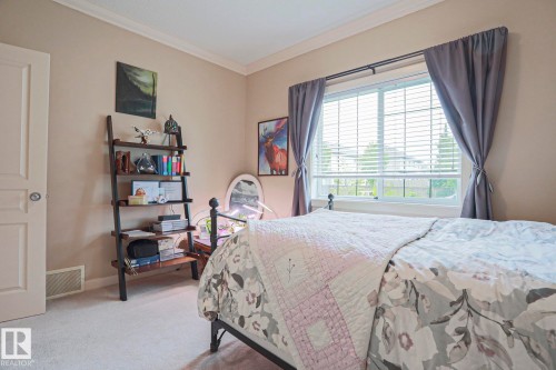 Bright bedroom featuring soft carpet flooring, a large window with white blinds, and crown molding - 13 7293 South Terwillegar Drive, Edmonton, AB 