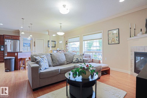 Open-concept living space featuring wood-finish flooring, a tiled fireplace, and multiple windows - 13 7293 South Terwillegar Drive, Edmonton, AB 