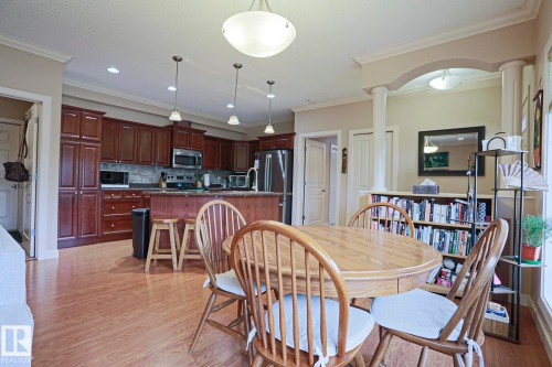 Kitchen and dining area featuring wood-finish flooring, dark wood cabinetry, stainless steel appliances, and a kitchen island with bar seating - 13 7293 South Terwillegar Drive, Edmonton, AB 