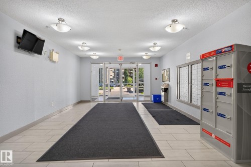Spacious interior corridor with light-toned tile flooring and flush-mounted ceiling light fixtures - 205 11816 22 Avenue, Edmonton, AB 