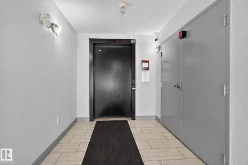 Hallway featuring light-toned square tile flooring with a dark area rug - 205 11816 22 Avenue, Edmonton, AB 