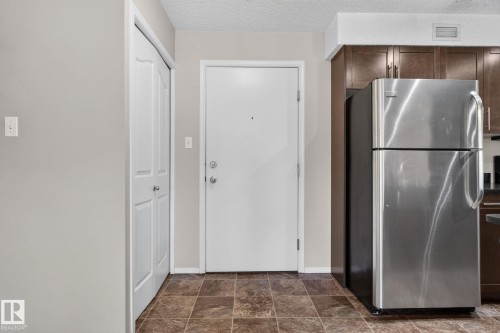 Entryway featuring a white door, brown tile-look flooring, and a stainless steel refrigerator - 205 11816 22 Avenue, Edmonton, AB 