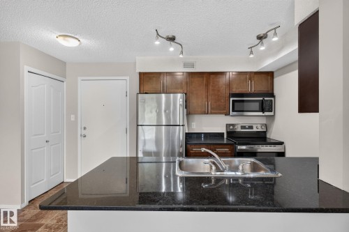 Kitchen featuring dark wood-finish cabinetry, stainless steel appliances, and black countertops - 205 11816 22 Avenue, Edmonton, AB 