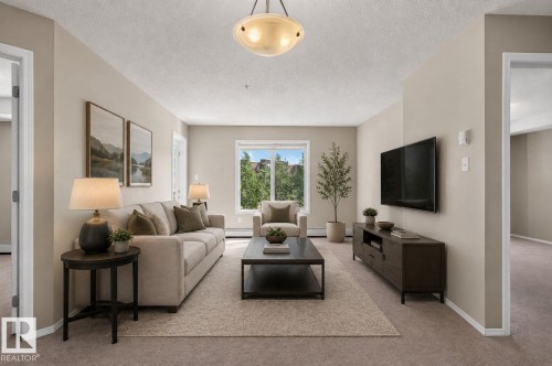 Spacious living area featuring neutral-toned walls, plush carpeting, and a central ceiling light fixture - 205 11816 22 Avenue, Edmonton, AB 