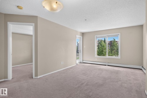 Spacious room with neutral-toned carpeting and light beige walls - 205 11816 22 Avenue, Edmonton, AB 