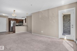 Open-concept living space featuring neutral carpeting, a light beige wall color, and direct access to an exterior patio with stone veneer - 