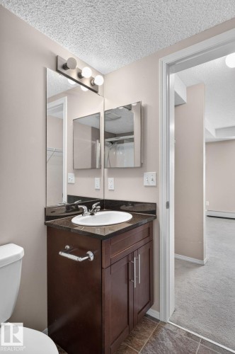 Bathroom vanity featuring a dark wood-finish cabinet with silver-tone hardware, an undermount sink, and a dark stone-finish countertop - 205 11816 22 Avenue, Edmonton, AB 
