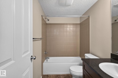 Full bathroom featuring a tub/shower combination with tile surround, a dark wood-finish vanity with a dark countertop, and a white porcelain sink - 205 11816 22 Avenue, Edmonton, AB 