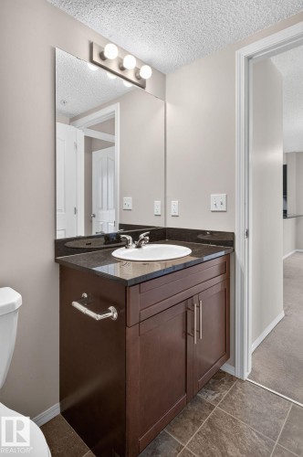 Bathroom vanity featuring dark wood-finish cabinetry, a black stone countertop, and an undermount sink with chrome fixtures - 205 11816 22 Avenue, Edmonton, AB 