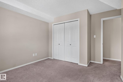 Expansive room featuring neutral-toned walls, plush carpeting, and a bi-fold closet with white paneled doors - 205 11816 22 Avenue, Edmonton, AB 