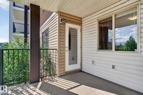 Balcony featuring a concrete surface, black metal railings, and a white paneled glass door - 205 11816 22 Avenue, Edmonton, AB 
