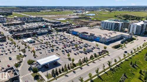Expansive retail center featuring a large asphalt parking area, surrounding commercial buildings, and multi-story residential structures - 205 11816 22 Avenue, Edmonton, AB 