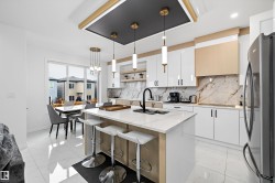 Gourmet kitchen featuring a central island with countertop seating, high-gloss white cabinetry, gold-tone accents, and a full-height marble-look backsplash - 
